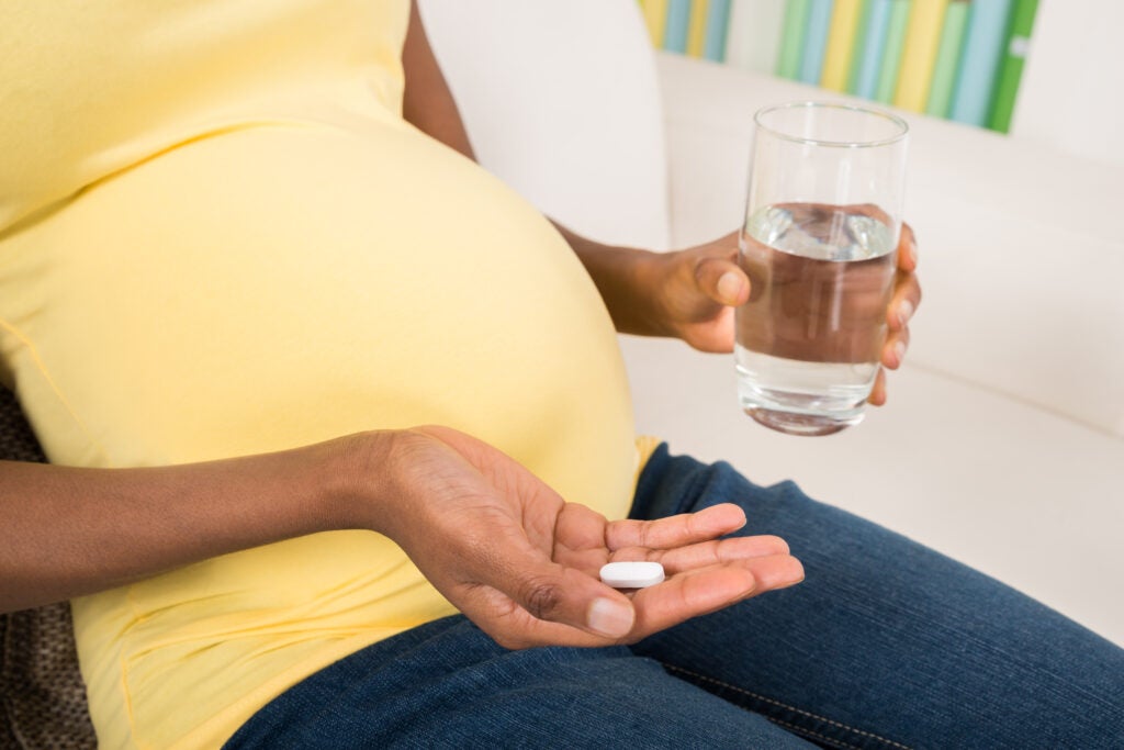 Close-up of pregnant woman holding glass of water and pill.